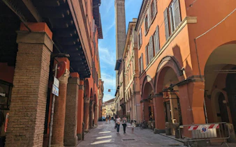Bologna street with historic porticoes and tower, part of self-guided city exploration game.