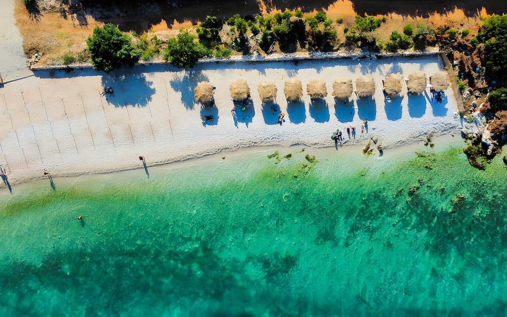 Aerial view of a beach with straw umbrellas and turquoise water in Vlora, Albania.