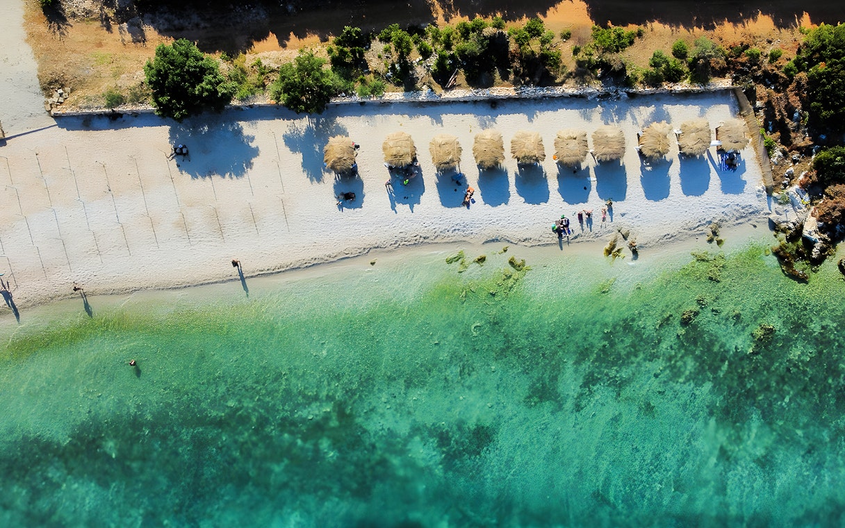 Aerial view of a beach with straw umbrellas and turquoise water in Vlora, Albania.