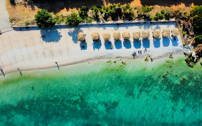 Aerial view of a beach with straw umbrellas and turquoise water in Vlora, Albania.