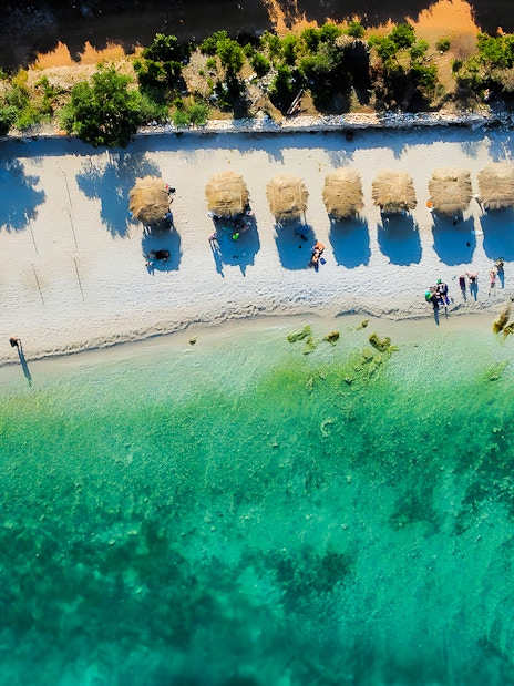 Aerial view of a beach with straw umbrellas and turquoise water in Vlora, Albania.