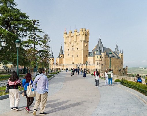 Visitors walking towards the Alcázar of Segovia, Spain, with its distinctive towers.