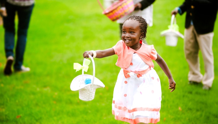 Girl running in park with basket of Easter eggs, celebrating Easter event.