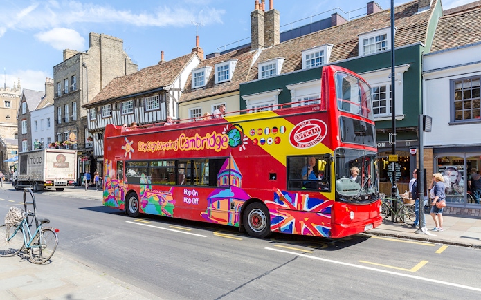 Double-decker bus on Cambridge Hop-On Hop-Off Tour passing historic buildings.