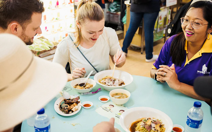 Tourists enjoying local dishes on a guided Michelin and hawker food tour.