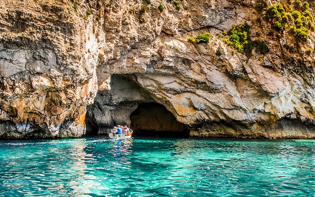Boat entering Blue Grotto cave, Malta, with clear turquoise water.