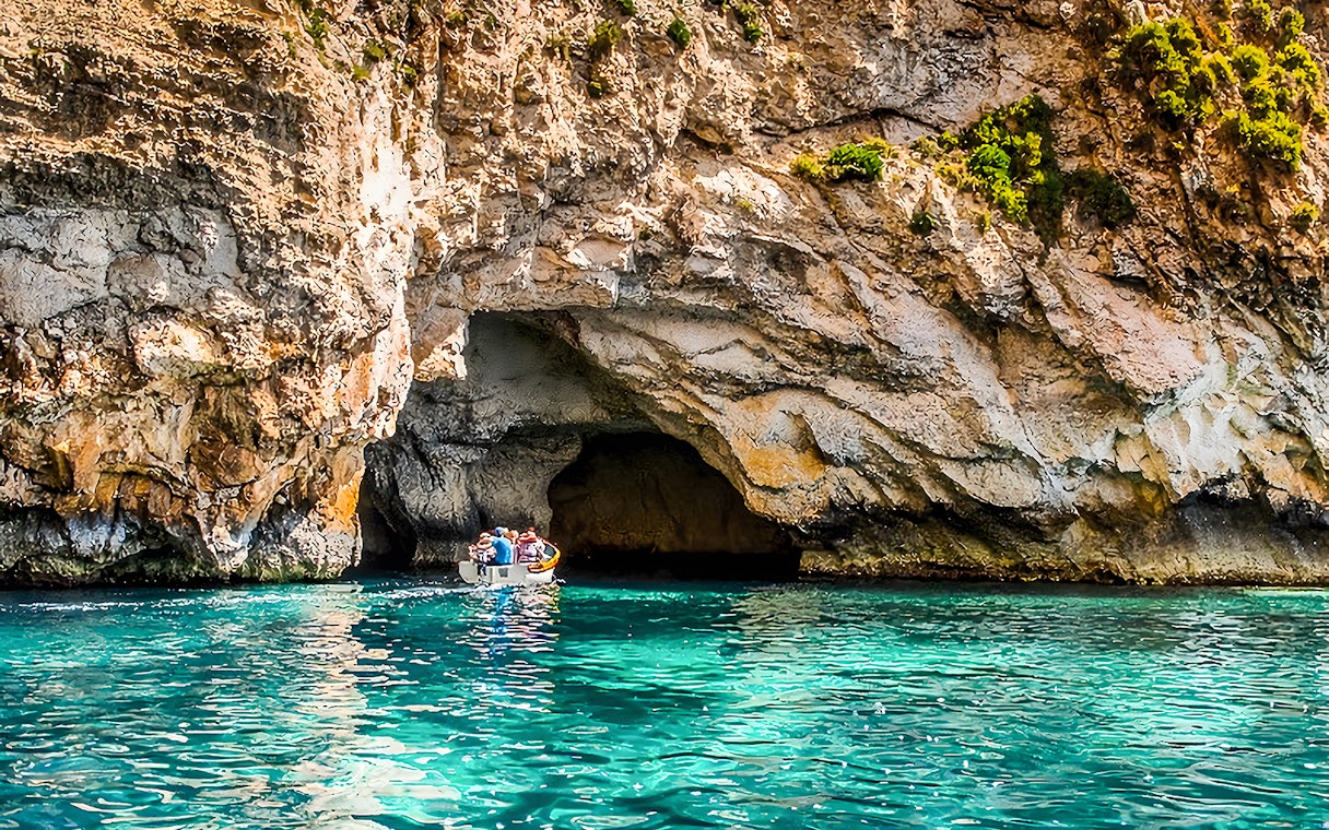 Boat entering Blue Grotto cave, Malta, with clear turquoise water.