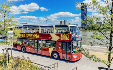 Tourists on Big Bus Vienna passing by the Danube River with city skyline in view.