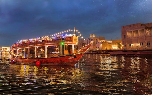 Pirate ship dhow cruise with lights on water at night, cityscape in background.