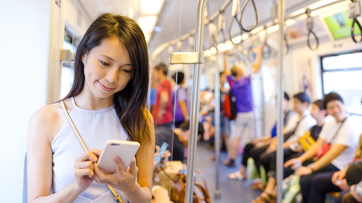 Woman using smartphone inside a metro carriage with seated passengers.