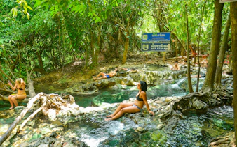 Visitors relaxing in the Emerald Pool Hot Springs surrounded by lush greenery in Krabi, Thailand.