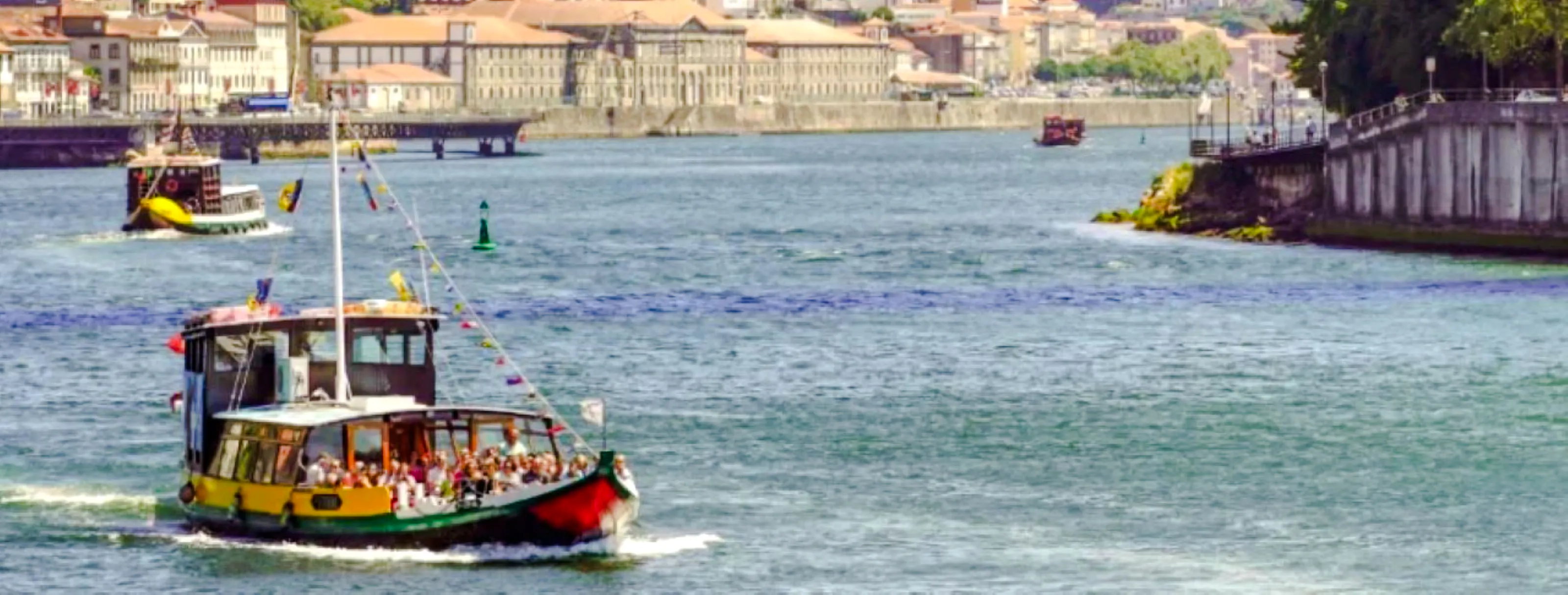 Boat cruising on the Douro River in Porto with cityscape in the background.