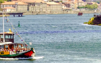 Boat cruising on the Douro River in Porto with cityscape in the background.