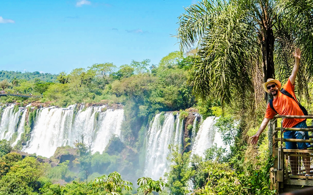 Tourist posing on a platform with Iguazu Falls in the background, Argentina.