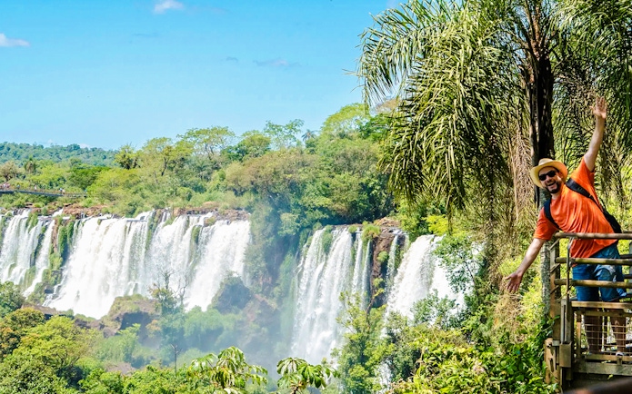 Tourist posing on a platform with Iguazu Falls in the background, Argentina.