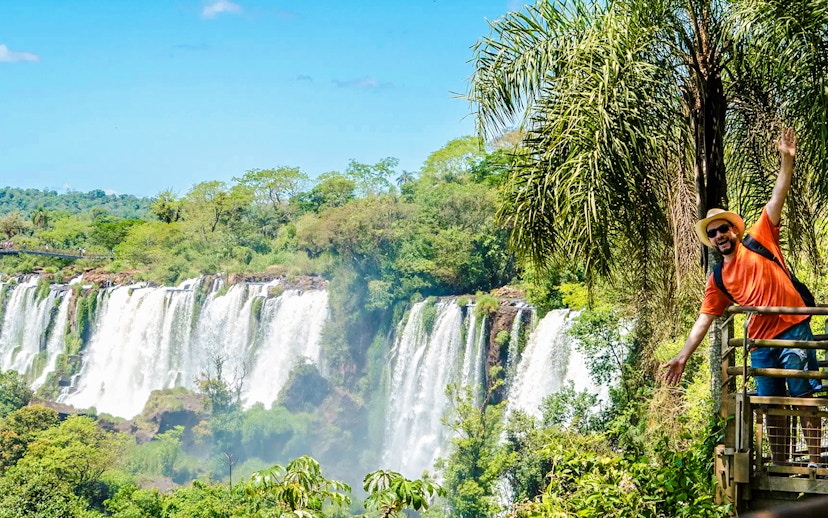 Tourist posing on a platform with Iguazu Falls in the background, Argentina.