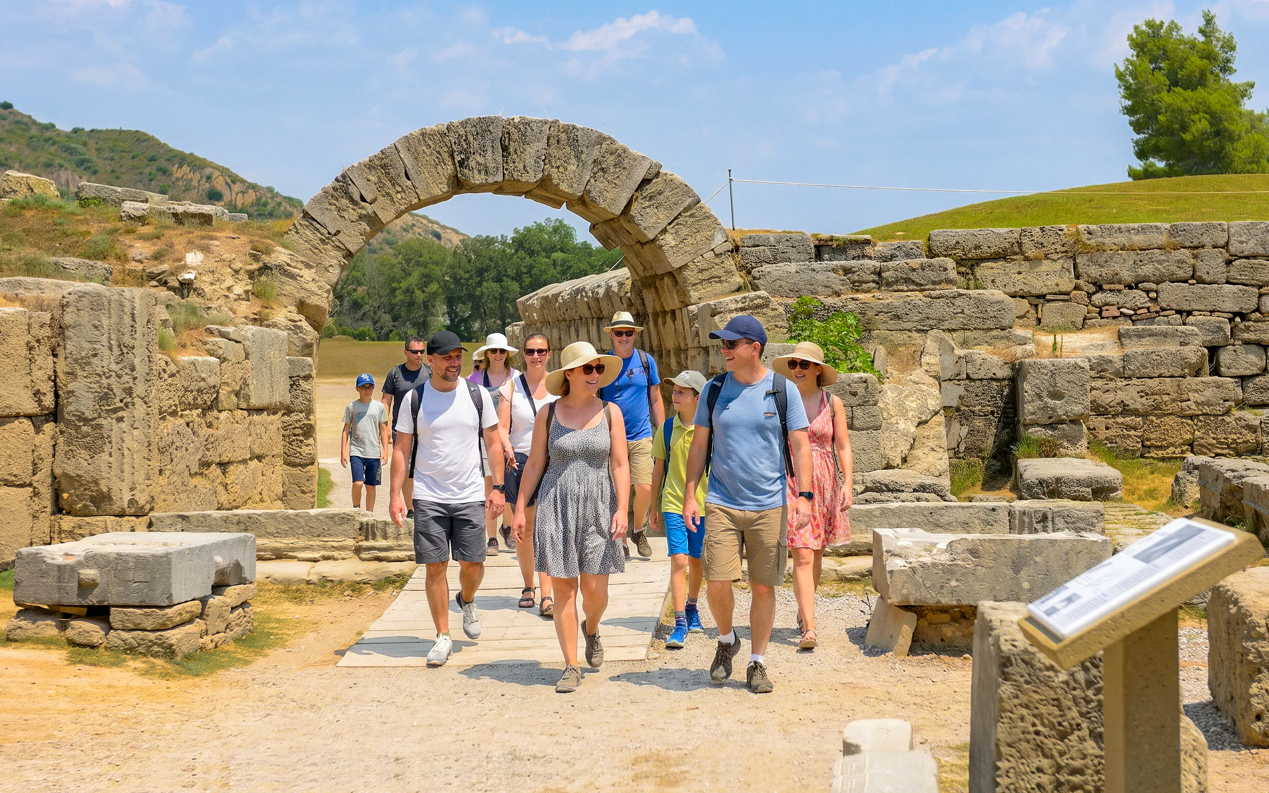 Visitors walking through ancient stone archway at Olympia Stadium, Greece.