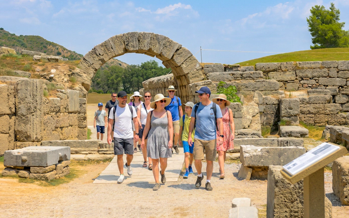 Visitors walking through ancient stone archway at Olympia Stadium, Greece.