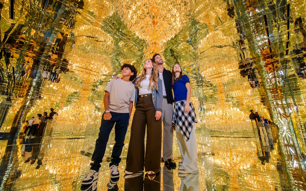 Family exploring mirrored room with golden lights at House Of Hype.