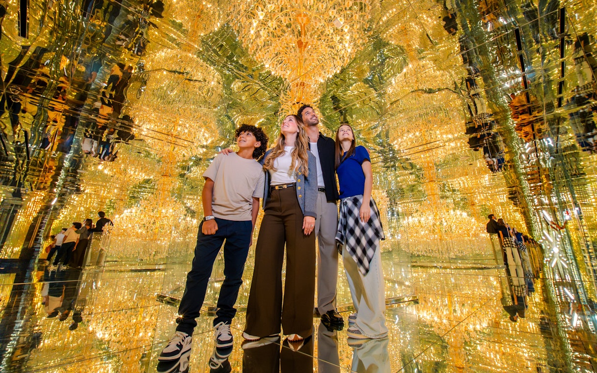 Family exploring mirrored room with golden lights at House Of Hype.