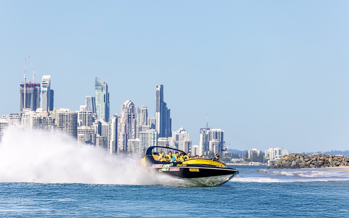 Jet boat speeding on water with city skyline in the background, Gold Coast.