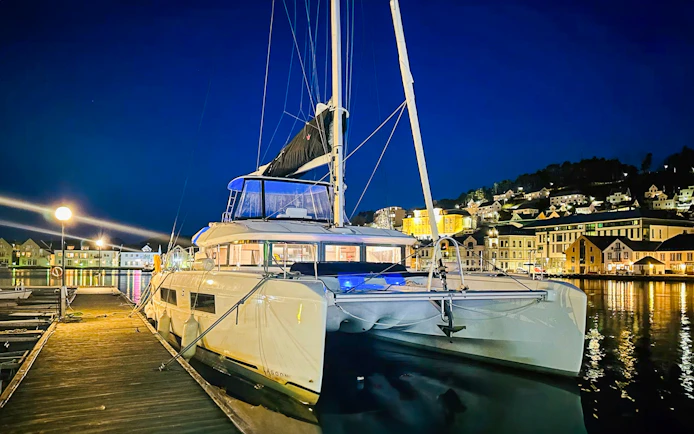 Luxury Catamaran Arctic Princess docked at night in a scenic harbor.