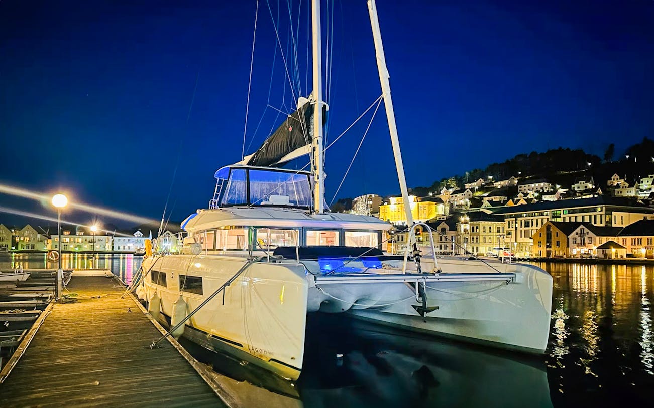 Luxury Catamaran Arctic Princess docked at night in a scenic harbor.