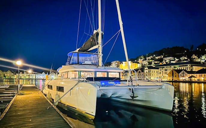 Luxury Catamaran Arctic Princess docked at night in a scenic harbor.