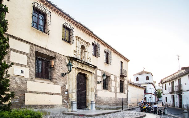 Historic building and street in the Albaicín district, Granada, with people dining outdoors.