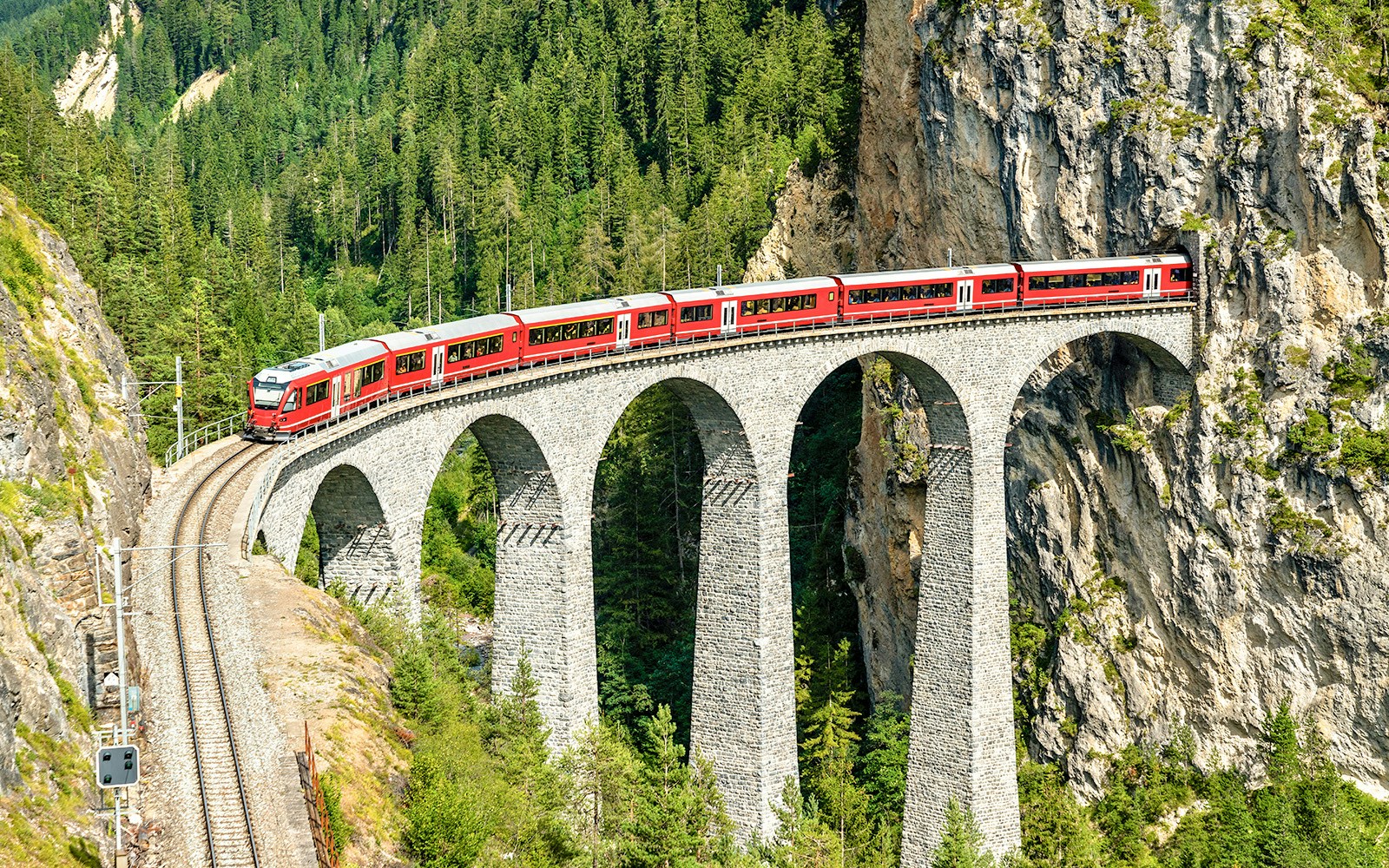 Train crossing six arched limestone pillars of Landwasser Viaduct in Switzerland.