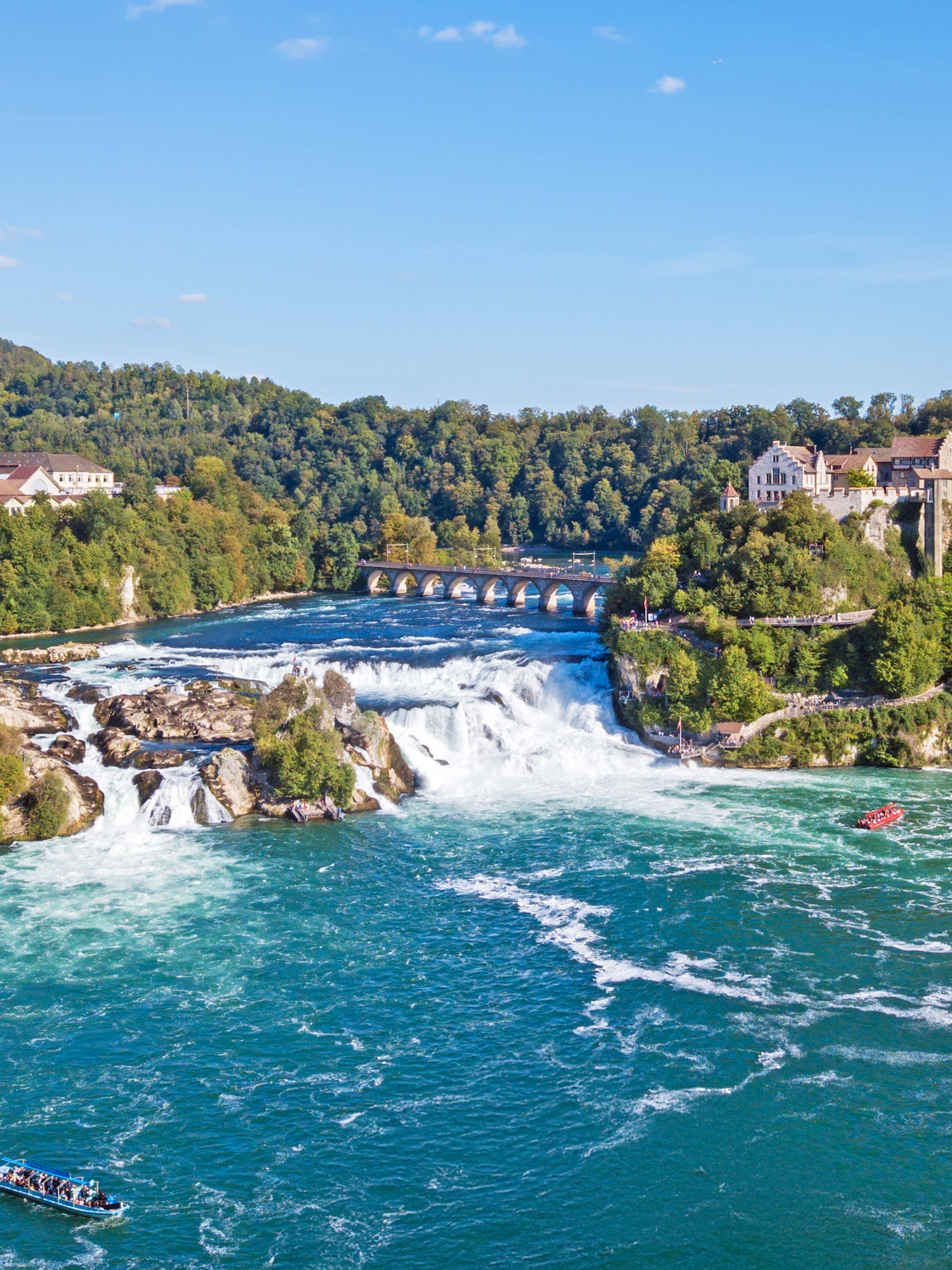 Panoramic aerial view of Rhine Falls, Switzerland, with surrounding buildings and lush greenery.