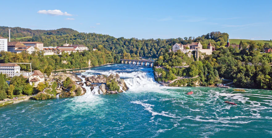 Panoramic aerial view of Rhine Falls, Switzerland, with surrounding buildings and lush greenery.