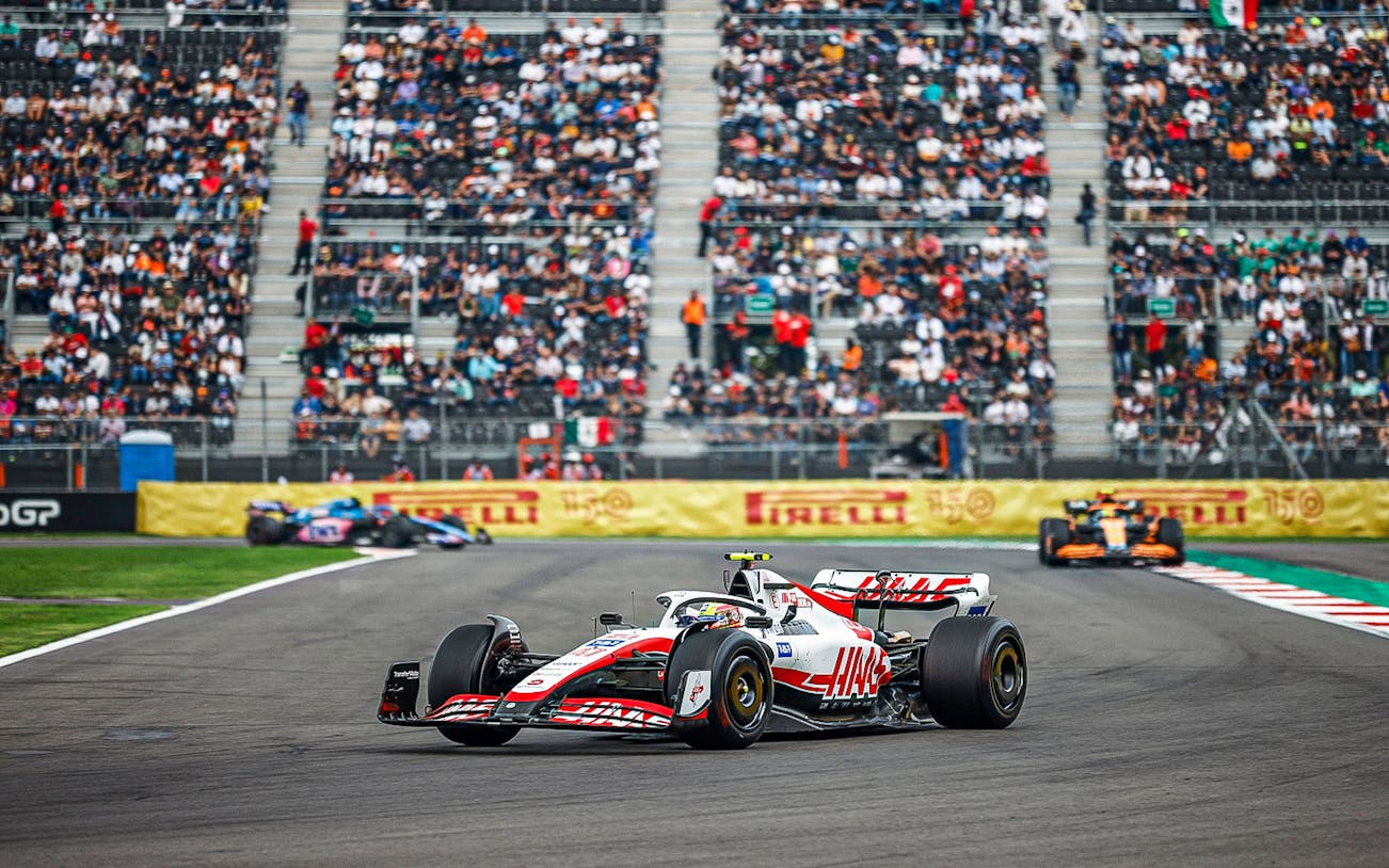 Race cars on track at Formula 1 Mexico Grand Prix with spectators in the stands.