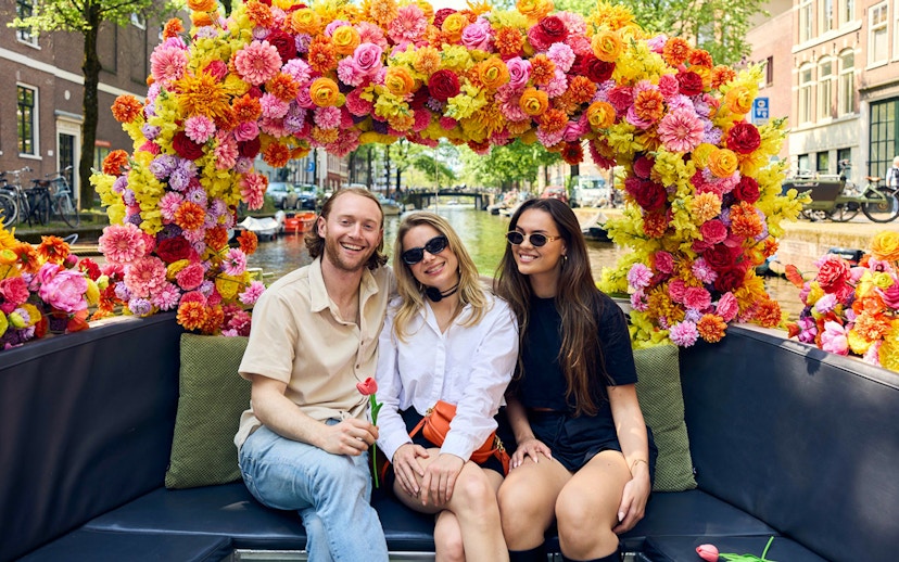 Group enjoying Amsterdam canal cruise on a flower-adorned boat.