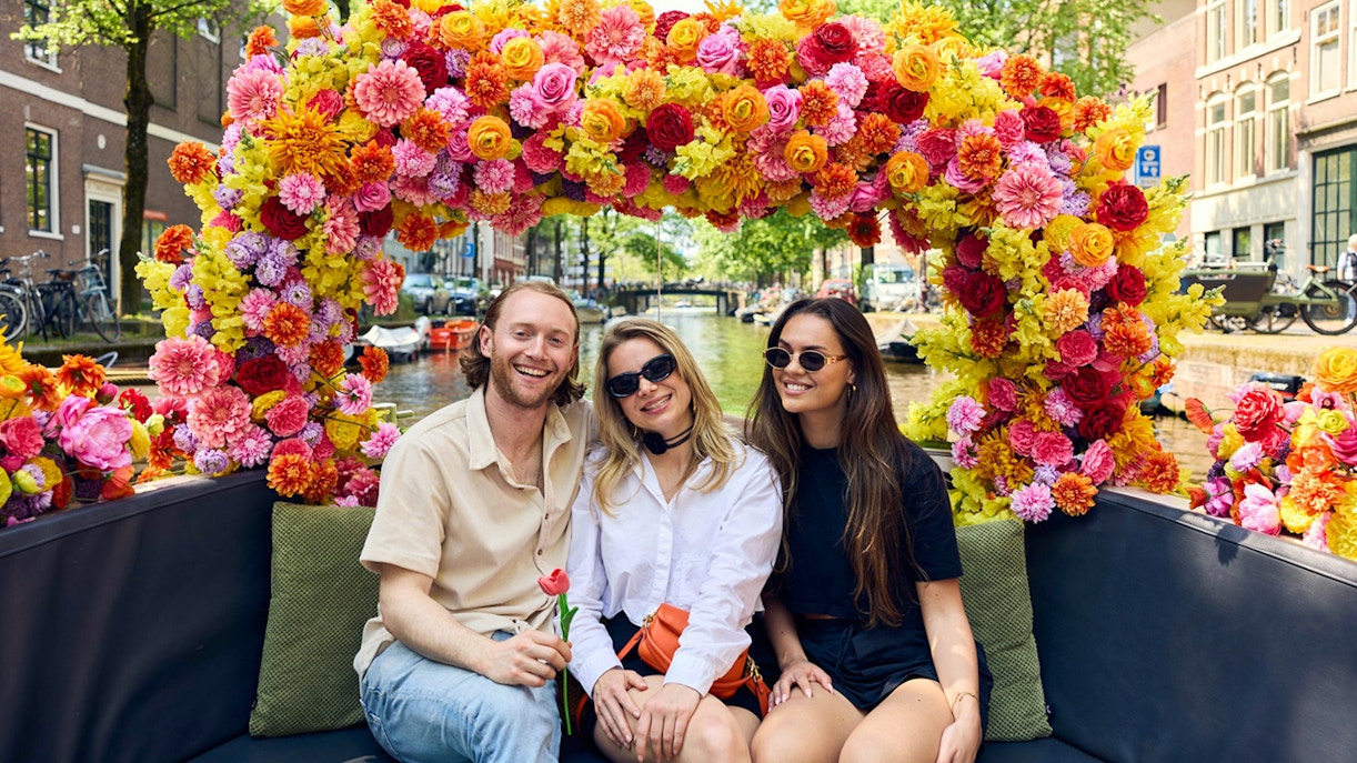 Group enjoying Amsterdam canal cruise on a flower-adorned boat.