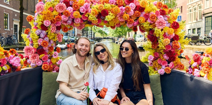 Group enjoying Amsterdam canal cruise on a flower-adorned boat.