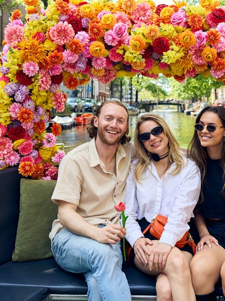 Group enjoying Amsterdam canal cruise on a flower-adorned boat.