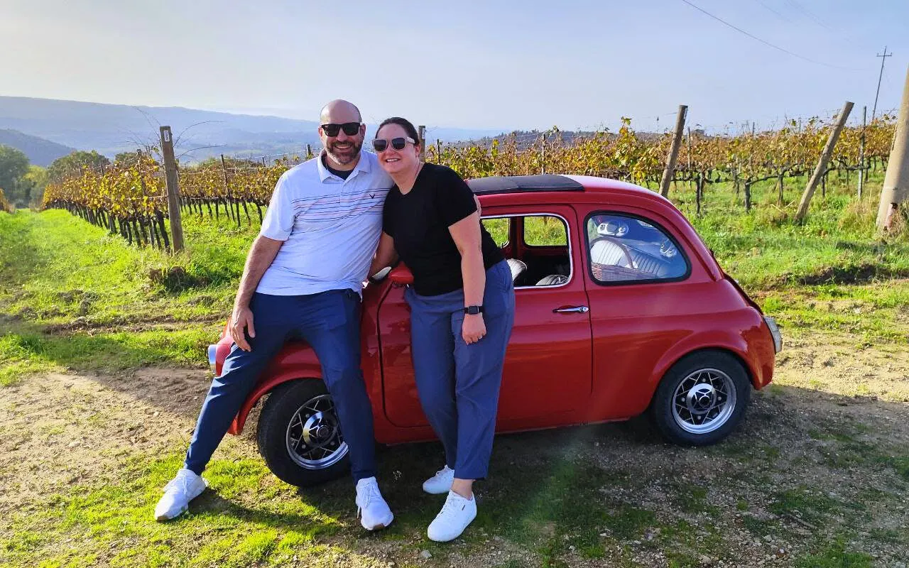 Couple with vintage Fiat 500 in Chianti vineyard during sunset drive.