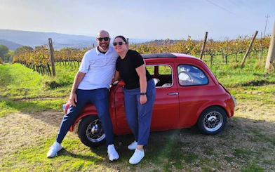 Couple with vintage Fiat 500 in Chianti vineyard during sunset drive.