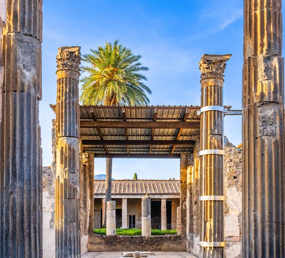 Ancient ruins with columns and palm tree in Pompeii, Italy, part of Sorrento to Pompeii tours.