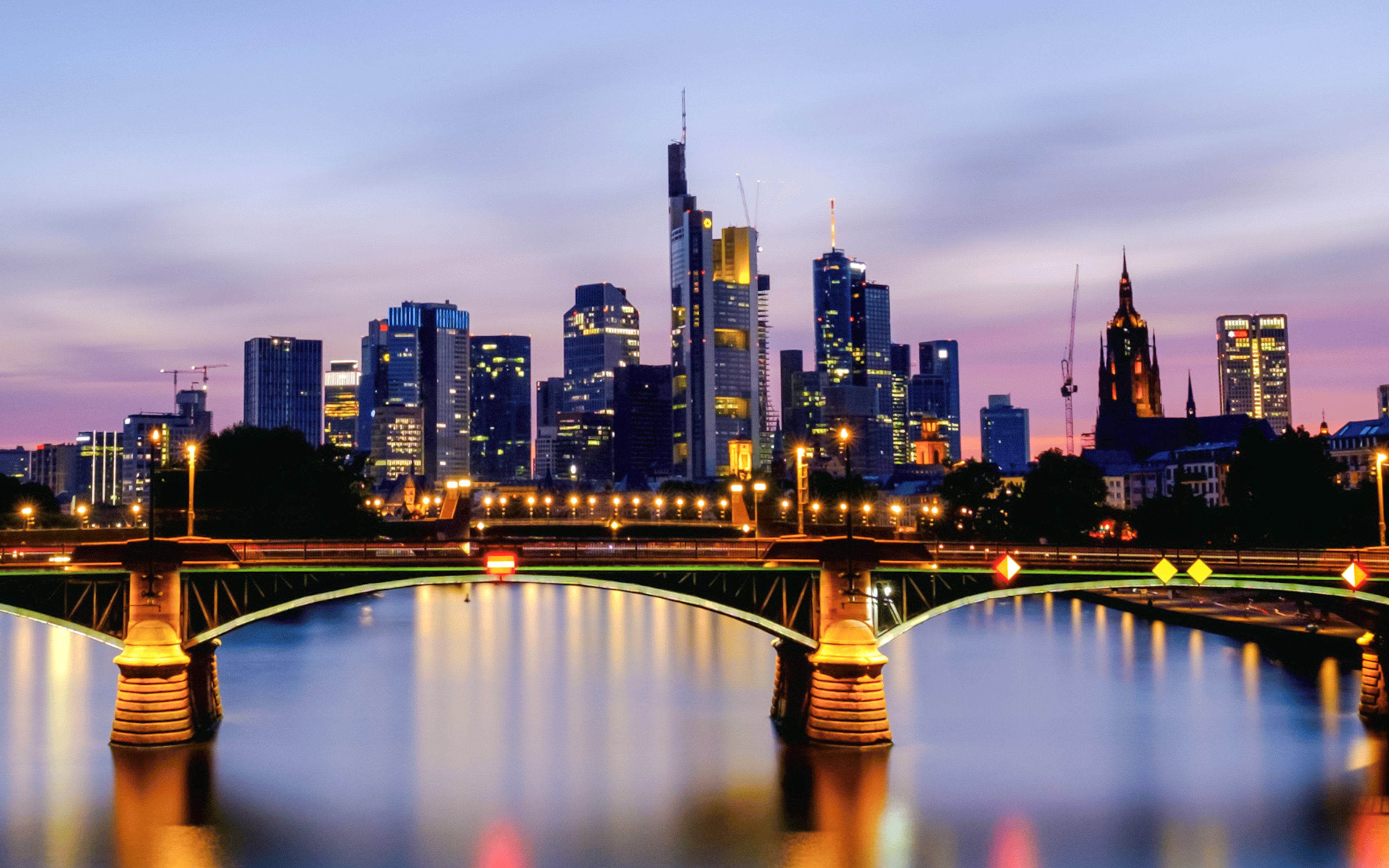 Frankfurt's Iron Bridge illuminated at night with city skyline in the background.