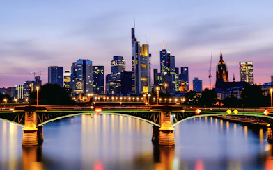 Frankfurt's Iron Bridge illuminated at night with city skyline in the background.