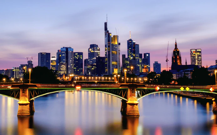 Frankfurt's Iron Bridge illuminated at night with city skyline in the background.