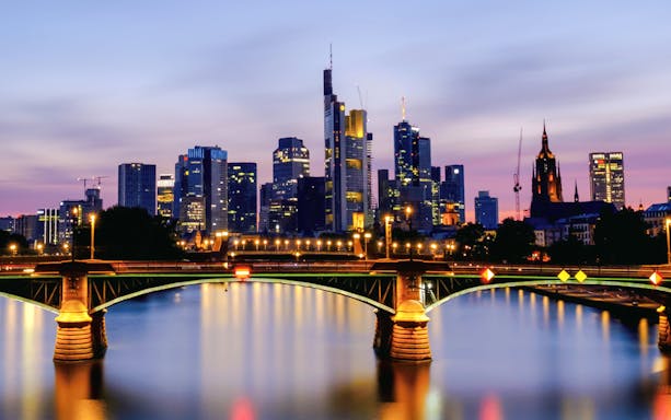 Frankfurt's Iron Bridge illuminated at night with city skyline in the background.