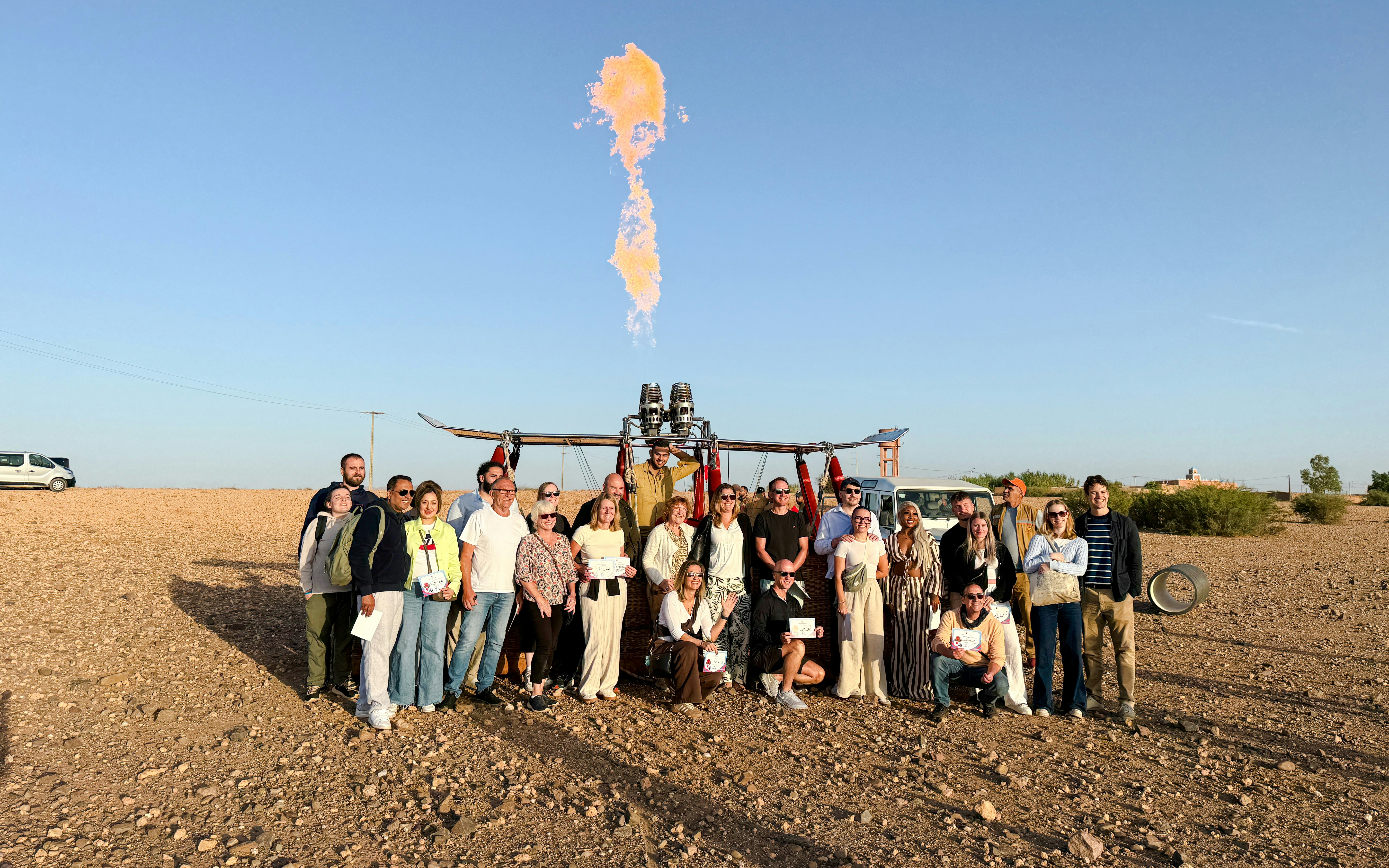 Group posing with hot air balloon in Marrakech desert.