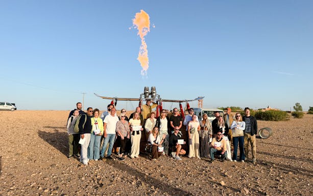 Group posing with hot air balloon in Marrakech desert.