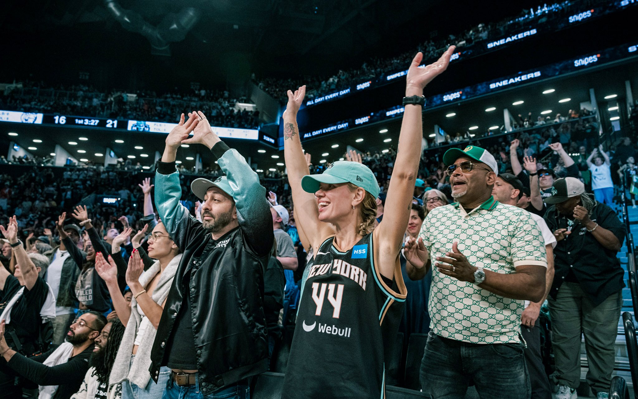 Fans cheering at New York Liberty basketball game in a lively arena.