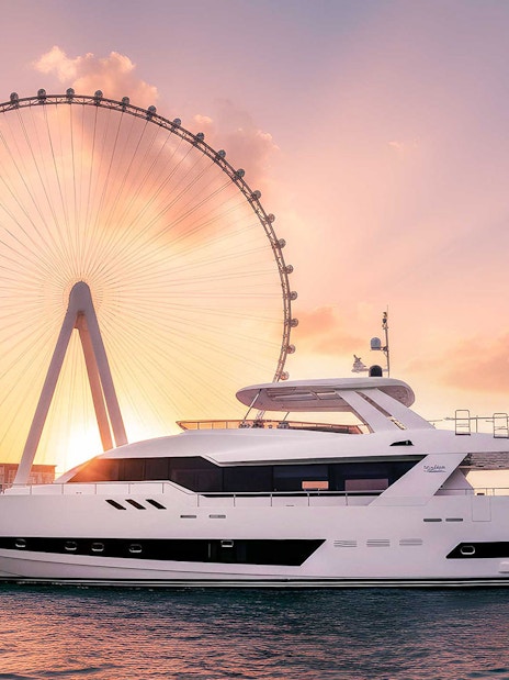 Yacht cruising near Ain Dubai Ferris wheel at sunset.