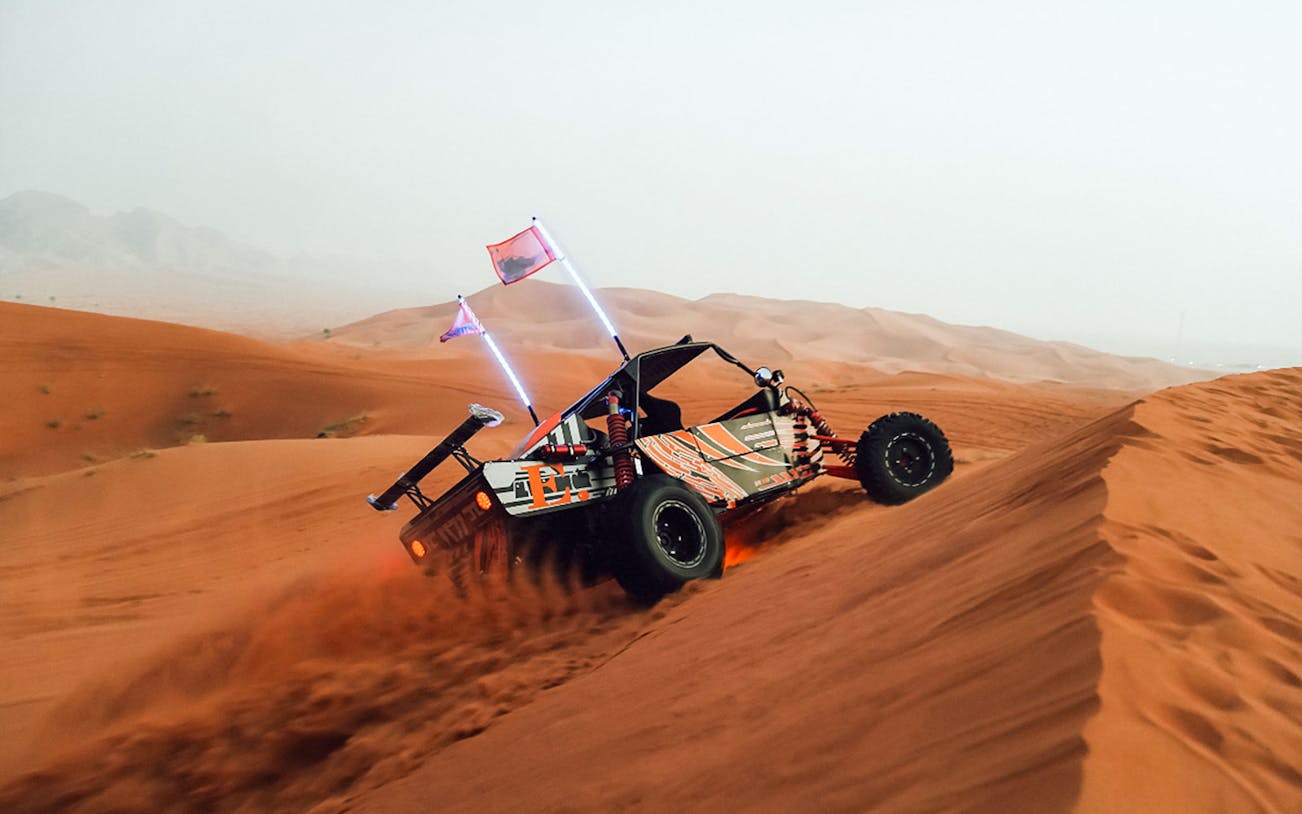 Dune buggy ascending a sand dune during a desert safari.