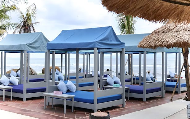 Private cabanas with blue canopies at Flamingo Beach Club overlooking the ocean.